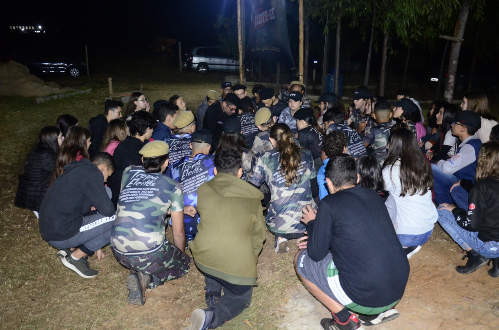 Servos da Comunidade Católica Apóstolos reunidos em círculo com os recrutas durante a noite do acampamento